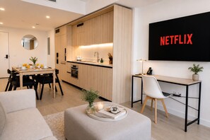 Moderni olohuone, jossa on ruokailutila, pieni keittiö ja seinälle asennettu televisio, jossa näkyy Netflix.