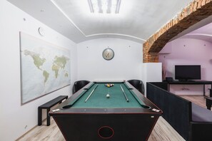 A pool table with a world map, a clock, and a brick arch in a room with a TV and seating. - Prague Group Stay for 20 • Billiard•Foosball•Darts (Praha)