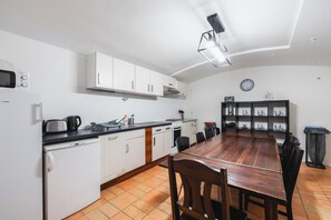 Eine kleine Küche mit weißen Schränken, einer schwarzen Arbeitsplatte, einem Holztisch und einer Uhr an der Wand.