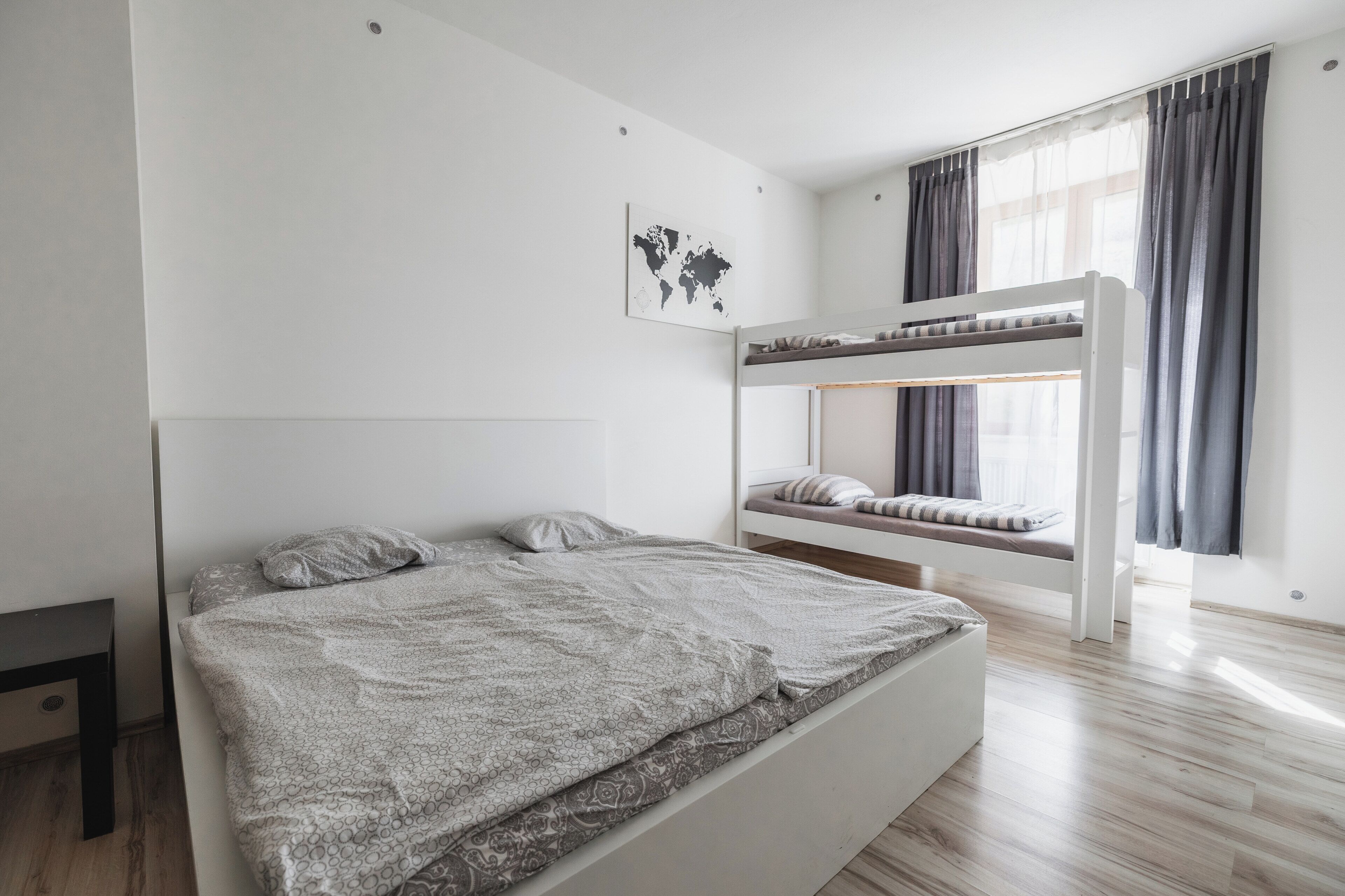 Ein Etagenbett mit gemustertem Bettbezug und Kissen, eine Weltkarte an der Wand und ein Fenster mit Vorhängen.