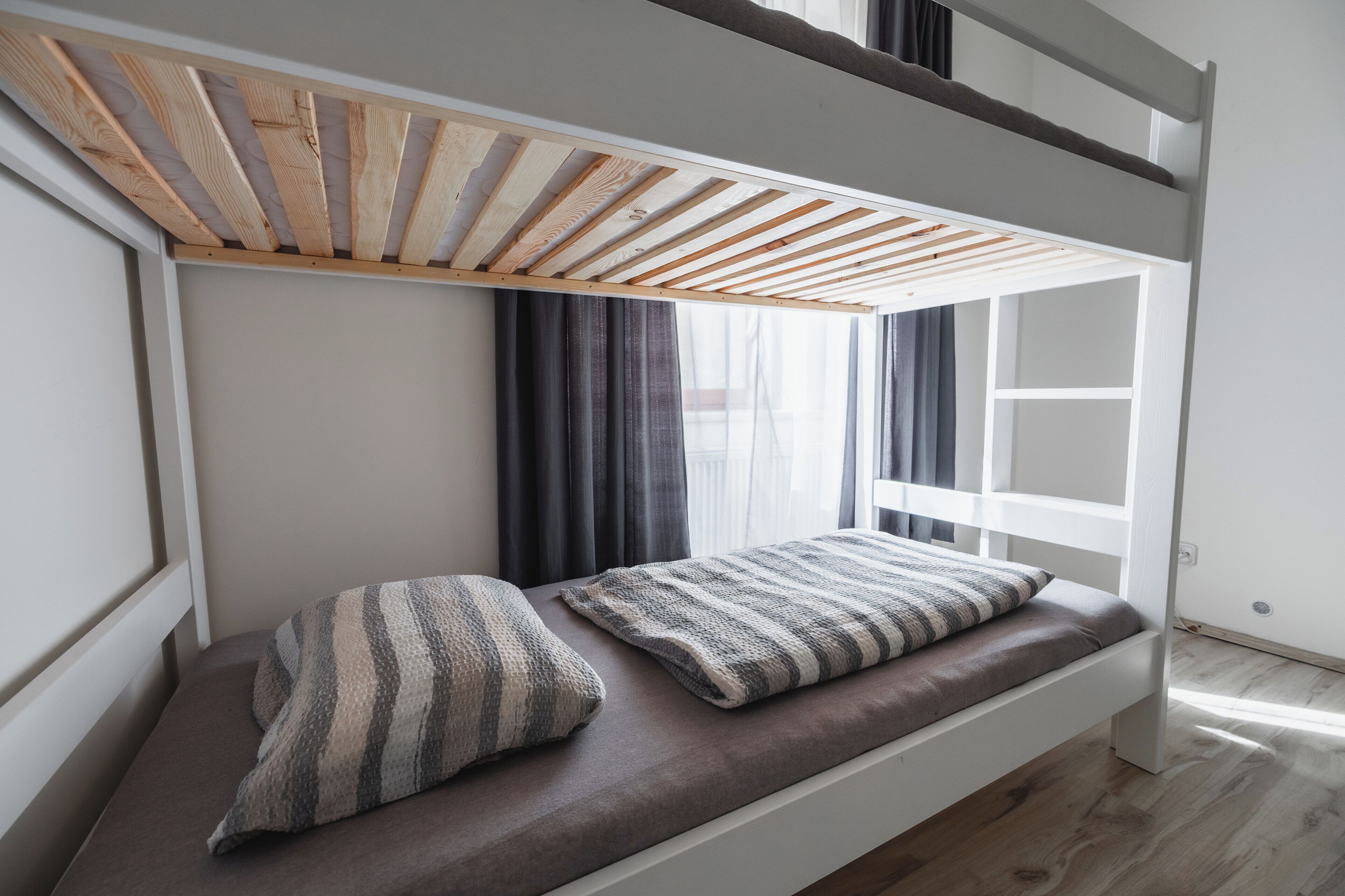 A bunk bed with a wooden slat ceiling, a window with curtains, and a cushion with a striped pattern.