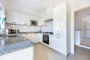 Eine moderne Küche mit weißen Schränken, einer Granit-Arbeitsplatte, einer integrierten Mikrowelle, einem Gasherd und einem Spülbecken.