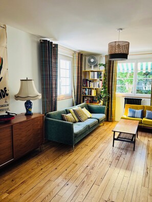 A living room with a sofa, a coffee table, a bookshelf, a lamp, and a fan. - Bright 3-bed garden house, 12 min walk to Bayonne (Bayonne)