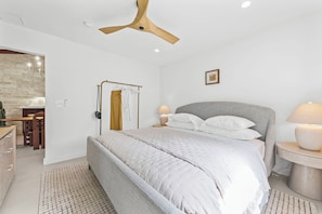 Ein modernes Schlafzimmer mit einem großen Bett, Nachttischlampen, einem Holzakustikventilator und Blick ins Badezimmer.