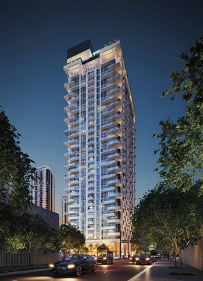 Un edificio alto con varios balcones, rodeado de árboles y una calle con coches.