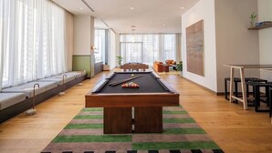 A pool table in a room with a sofa and a small table, large windows with curtains, and a plant on a shelf. - Modern 1BR with Pool Near Brickell & Downtown Miami (Miami)