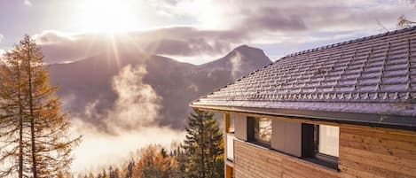 Un edificio moderno con techo inclinado, rodeado de un bosque y montañas al fondo.