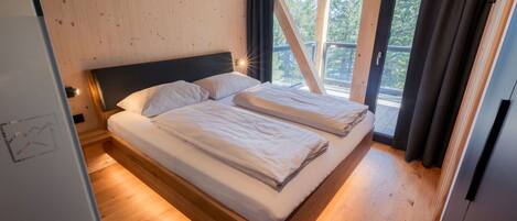 Uma cama de casal num quarto com paredes de madeira e uma janela grande.