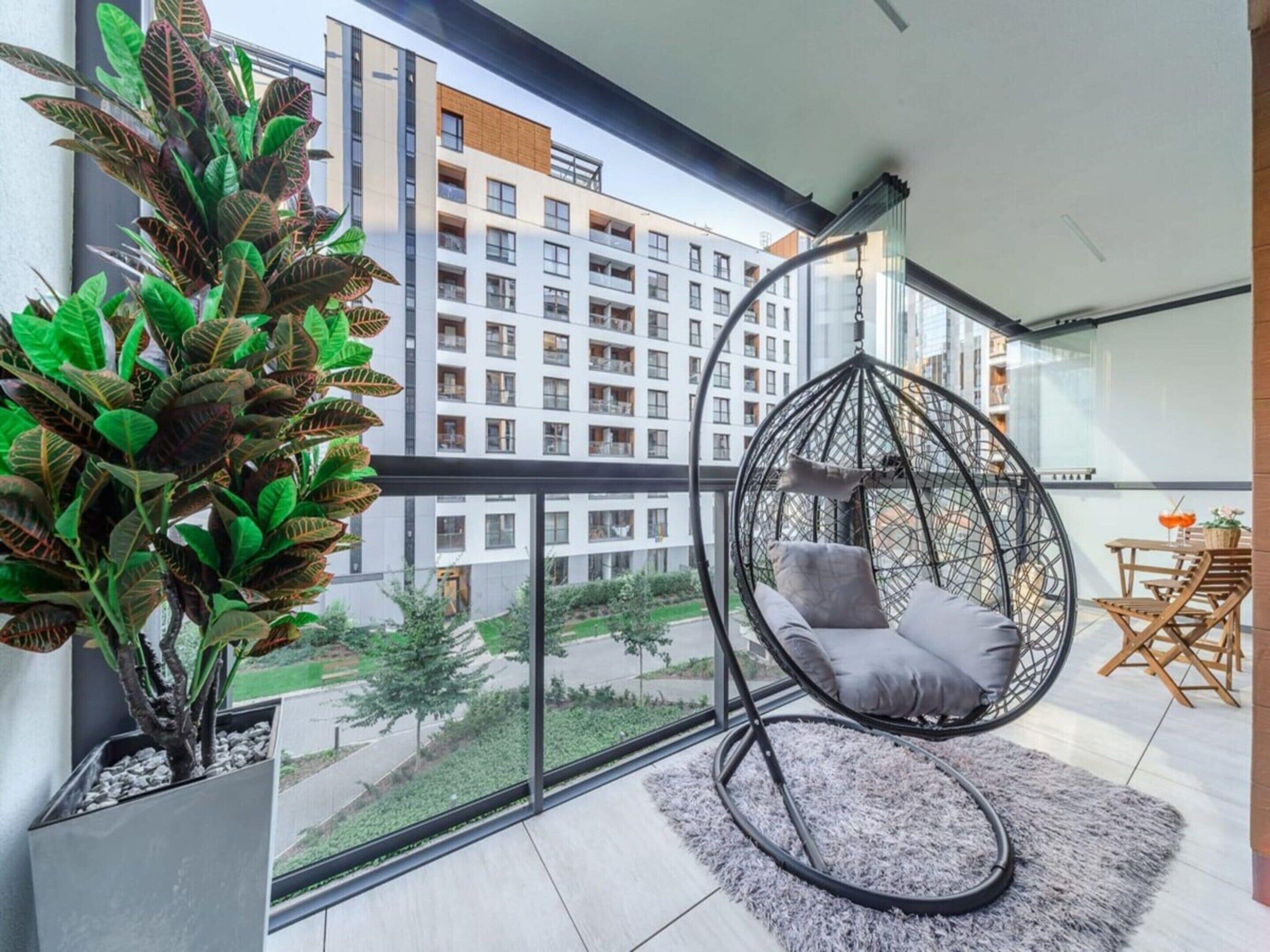Un appartement moderne avec un fauteuil suspendu, une plante en pot et une vue sur un immeuble d’habitation.