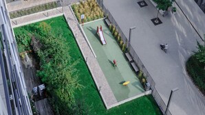 Eine Vogelperspektive eines Innenhofs mit grüner Rasenfläche, einem Spielplatz und einem Gebäude mit großen Fenstern.