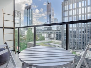 A modern balcony with a round table and chairs, overlooking a cityscape with high-rise buildings. - Warsaw Flat With Quiet Loggia (Warsaw)