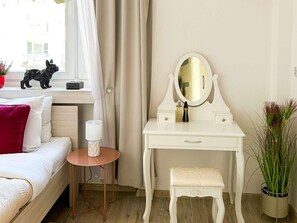 A bedroom with a bed, a small bedside table with a lamp, a white dresser with a mirror, and a window with curtains. - Lodz Apartment for 4 Guests (Łódź)