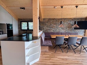 Eine moderne Küche mit einer zentralen Kochinsel, einem Essbereich mit Holztisch und Stühlen sowie einer Wand aus Stein im Hintergrund.
