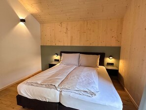 Ein Schlafzimmer mit Holzbalkendecke, einem Bett mit weißer Bettwäsche, zwei Nachttischen mit Lampen und einem grünen Kopfteil.