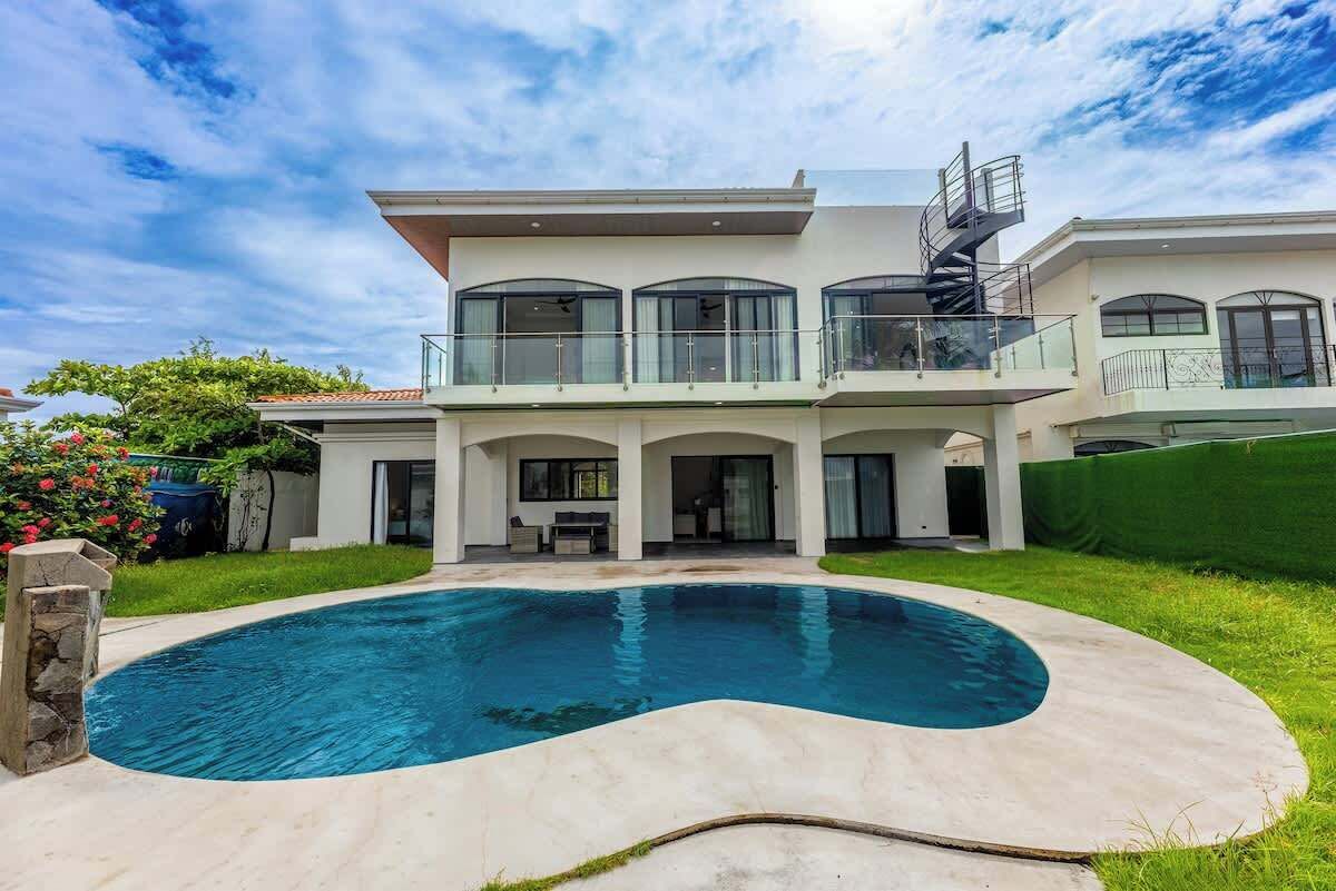 Une maison moderne à deux étages, dotée d’une piscine, d’un patio couvert et d’un escalier en colimaçon.
