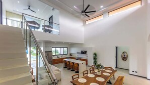 A modern kitchen with a central island, a dining area with a wooden table and benches, and a staircase leading to an upper level. - Villa Bajamar - Costa Rica (Bajamar)
