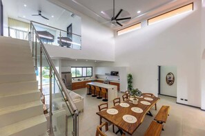 Eine moderne Küche mit Kochinsel, ein Essbereich mit Holztisch und Bänken sowie eine Treppe zu einer oberen Ebene.