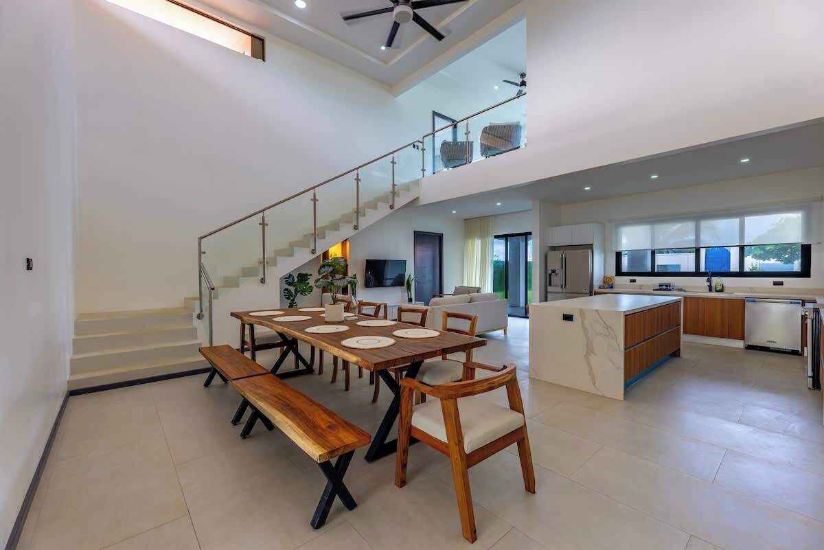 A spacious dining area with a high ceiling, a staircase leading to an upper level, and a modern kitchen with a large island.