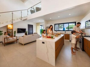 Eine geräumige, moderne Küche mit einer zentralen Kochinsel, ein Essbereich mit einer Couch und ein Wohnzimmer mit Fernseher.