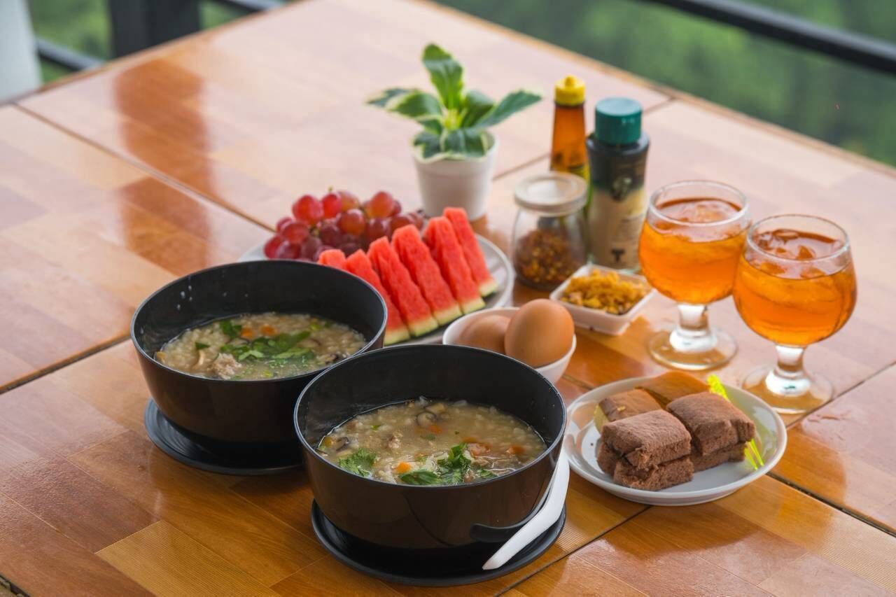 Una mesa con dos tazones de sopa, un plato de sandía en rodajas, un plato de pan, un cuenco pequeño de huevos y dos vasos de té.