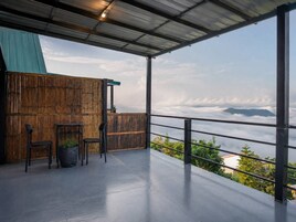Un balcón con vistas a nubes y follaje, una pared de bambú y una mesa con sillas.