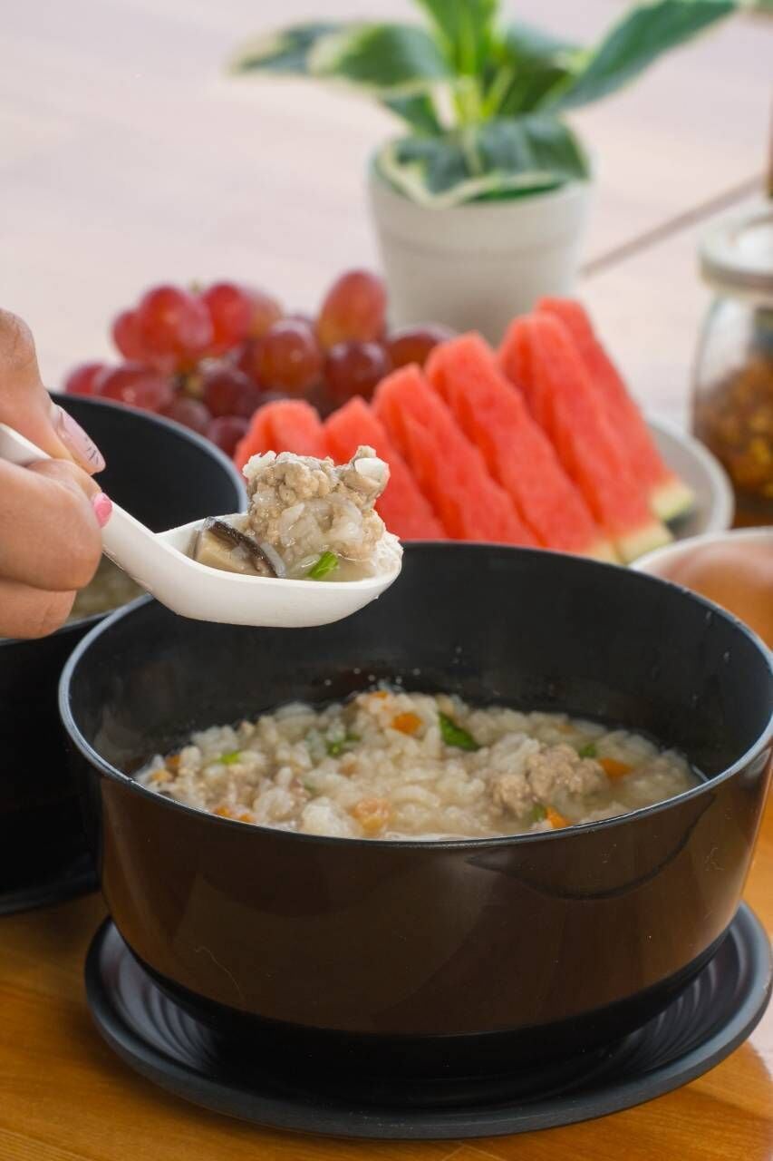 A bowl of soup with a spoonful being lifted, a plate of watermelon slices, and a bowl of grapes in the background.