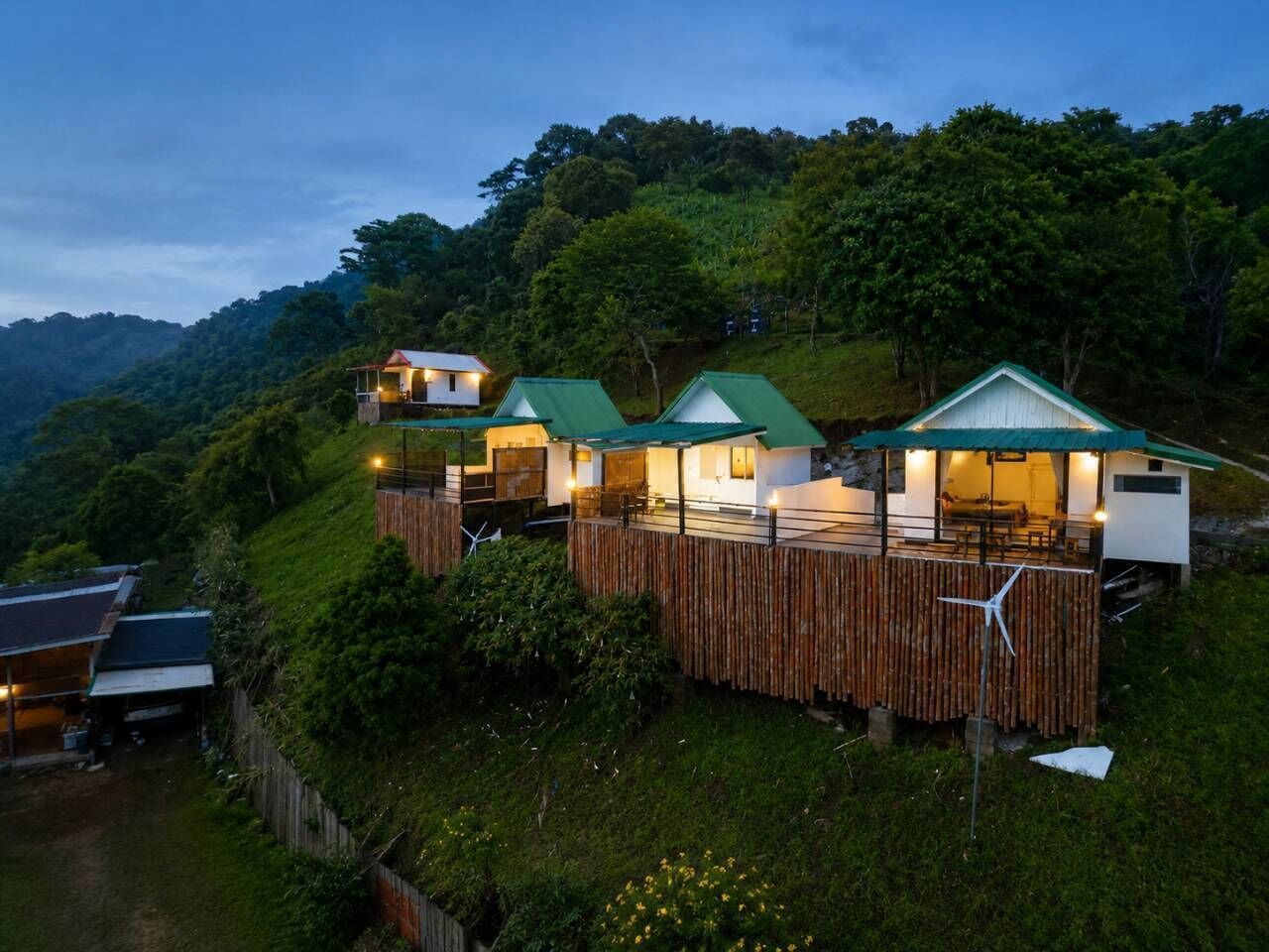 Una propiedad en una ladera con varias edificaciones, incluyendo una casa principal y varias construcciones más pequeñas, rodeada de abundante vegetación.