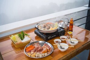 A hot pot setup with various meats and vegetables on a wooden table, a teapot, and condiments.