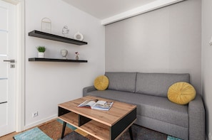 A modern living room with a grey sofa, two yellow cushions, a wooden coffee table with a magazine, and a wall-mounted shelf with decorative items. - House in Porspoder by Plage du Bourg Beach (Warsaw)