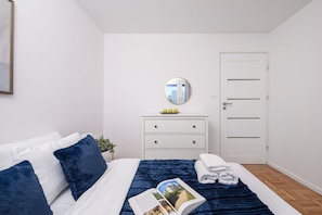 A bedroom with a bed, a bedside table with a mirror, a dresser, and a door. - Central City Apartment With Balcony in Warsaw (Warsaw)