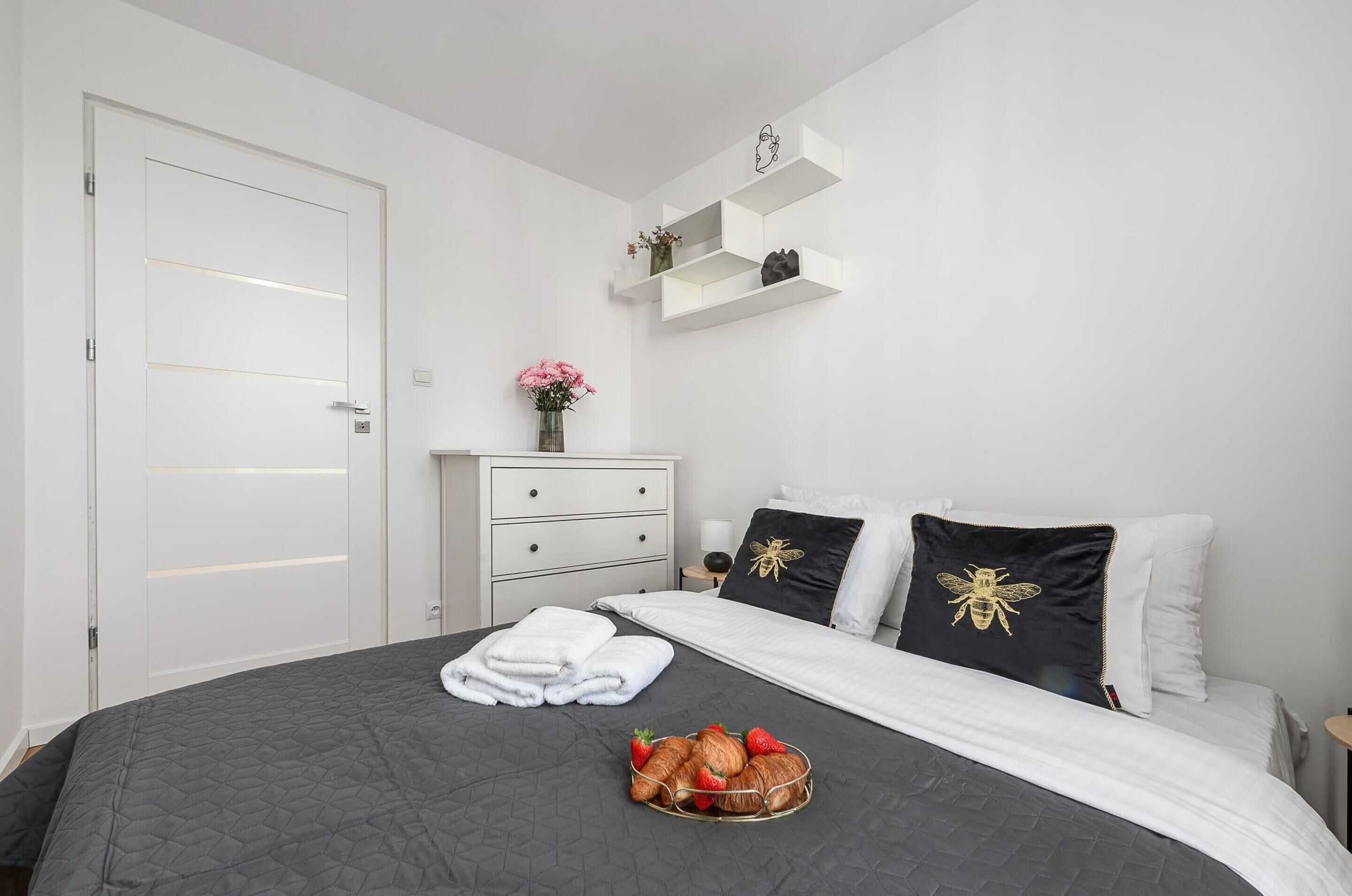 Un dormitorio con cama, cómoda, mesita de noche y estante de pared.