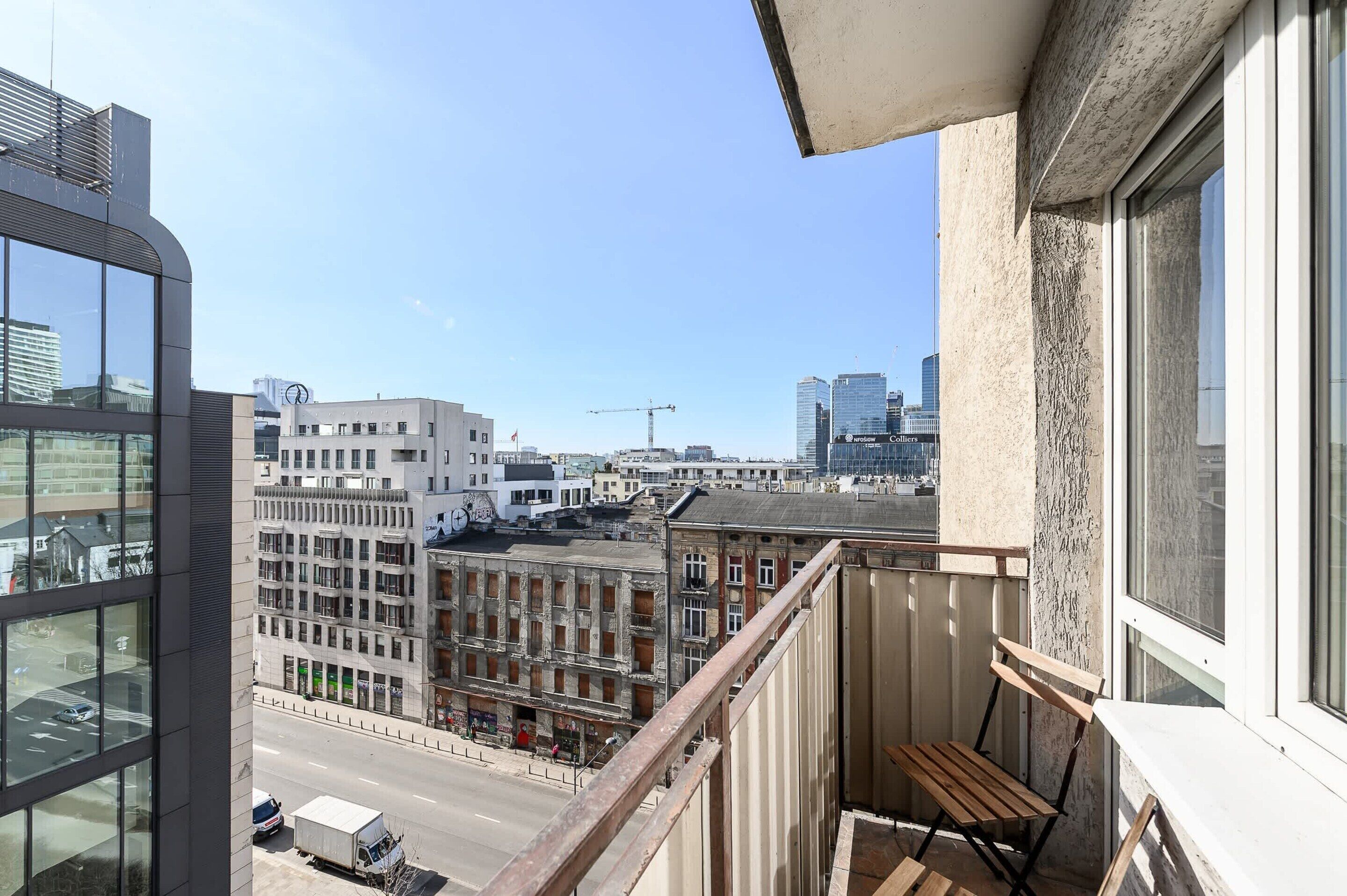 Varanda com vista para paisagem urbana, incluindo edifícios modernos e uma grua de construção.