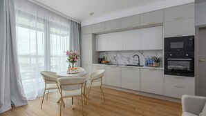 Uma cozinha moderna com armários brancos, um forno preto e uma área de jantar com mesa redonda e duas cadeiras.