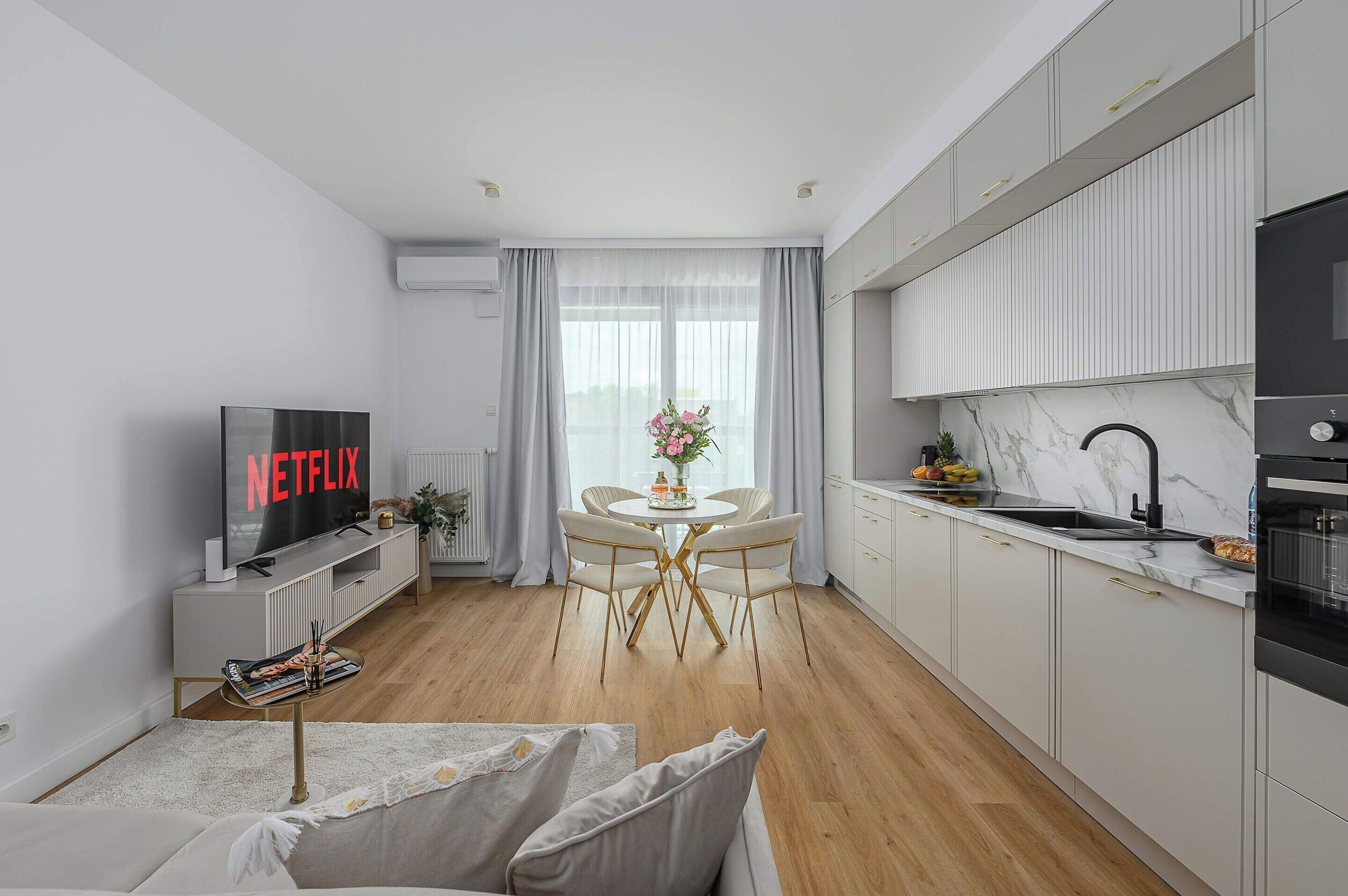 Eine moderne Küche mit Einbauofen, Essbereich mit Tisch und Stühlen sowie einem Fernseher, der 'NETFLIX' anzeigt.