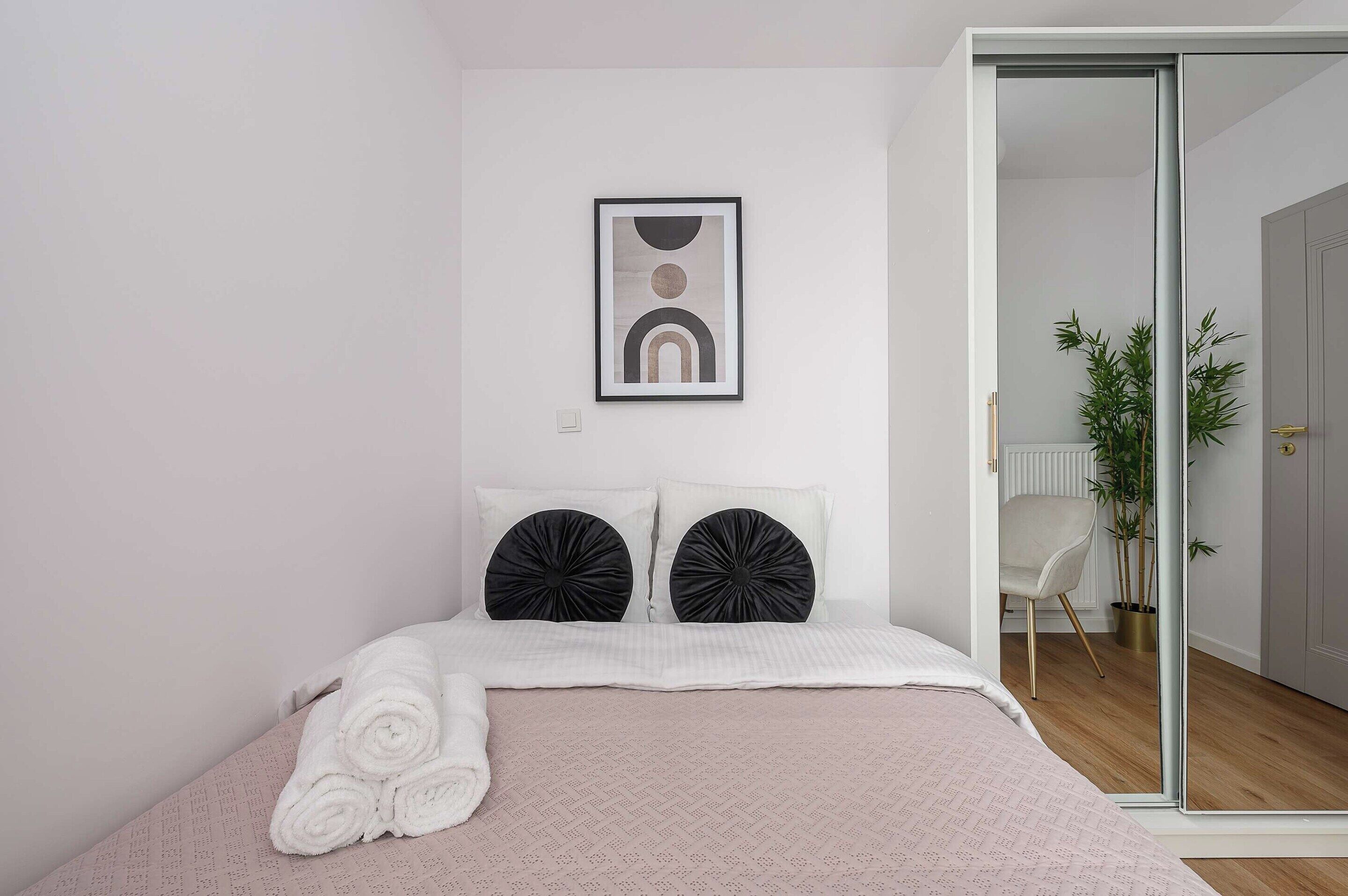 Quarto com cama, almofadas, um quadro emoldurado e uma porta que dá para outro cômodo.