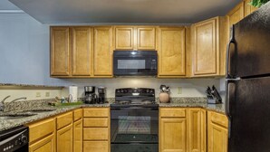 A kitchen with wooden cabinets, a black microwave, a stove, and a refrigerator.