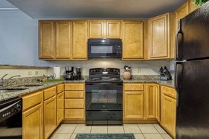 A kitchen with wooden cabinets, a black microwave, a stove, and a refrigerator.