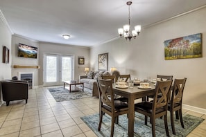 A dining area with a table set for four, surrounded by wooden chairs, a chandelier, and artwork on the walls.
