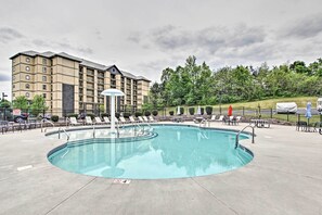 A hotel with a swimming pool, lounge chairs, and a covered patio area.