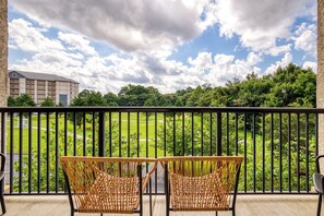 A balcony with two wicker chairs, a view of a green lawn, and a building in the background. - Gorgeous 3-bedroom condo with AC in welcoming Pigeon Forge! (Pigeon Forge)