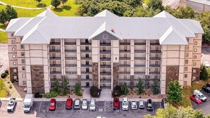 A multi-story hotel with a central entrance, parking lot, and surrounding greenery.