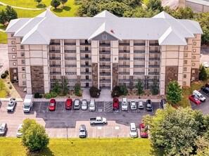 A multi-story hotel with a central entrance, parking lot, and surrounding greenery.