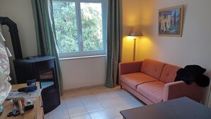 Una habitación con escritorio, sofá rosa, lámpara y ventana con cortinas.