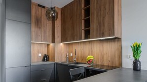 A modern kitchen with wooden cabinets, a built-in oven, a sink, and a dining area with a bench. - Quiet City Apartment for 4 (Łódź)