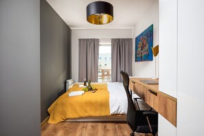 A modern hotel room with a bed, a desk, a chair, a painting, and a view of buildings outside. - City View Apartment in Warsaw (Łódź)