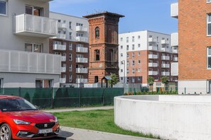 A modern apartment building with a red brick tower, balconies, and a red car parked in front. - City View Apartment in Warsaw (Łódź)