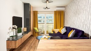A modern living room with a wooden dining table, a purple sofa with yellow cushions, and a view of the city through large windows. - City View Apartment in Warsaw (Łódź)