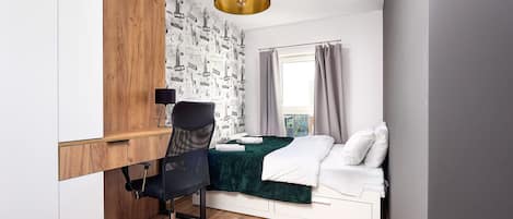 Un dormitorio con cama, escritorio y silla, ventana con cortinas y un papel tapiz con vistas a la ciudad.