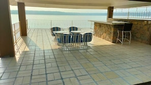 An outdoor patio with a table and chairs, a stone wall, and a view of the sea.