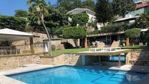 Una piscina con un muro de piedra y una zona de descanso con sillas.